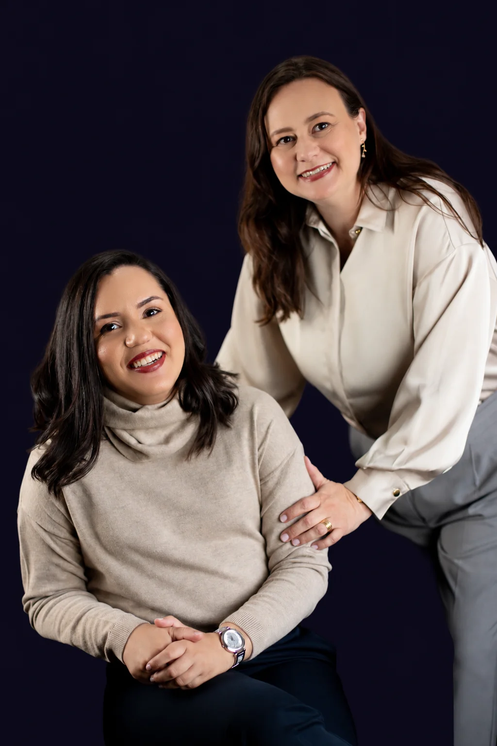 As duas instrutoras da imersão sorrindo, uma sentada e a outra em pé ao lado
